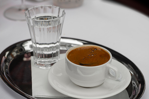 Turkish coffee in a white modern cup with a glass of water.