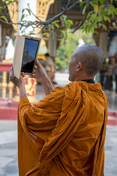 Mandalay, Myanmar - January 29, 2013: A Buddhist monk using a tablet to photograph the Kuthodew Pagoda in Mandalay, Myanmar (Burma).