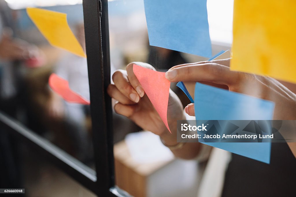 Hands of woman sticking adhesive notes on glass Close up shot of hands of woman sticking adhesive notes on glass wall in office Adhesive Note Stock Photo