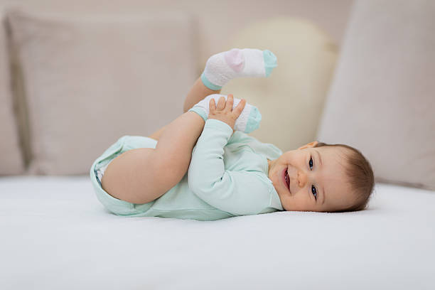 Playful baby lying down in bed Happy baby lying on white sheet and holding her legs 8 weeks stock pictures, royalty-free photos & images