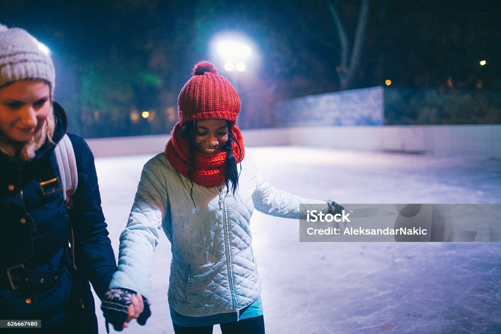 Learning to Ice-skate Photo of a cheerful friends learning how to ice-skate on Ice rink  Ice Rink Stock Photo