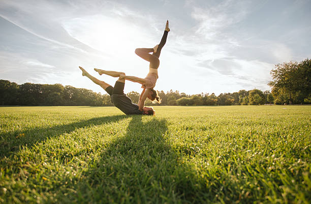 Healthy couple doing acro yoga on grass Healthy young couple doing acro yoga on grass. Man and woman doing various yoga poses in pair outdoors at the park. acroyoga stock pictures, royalty-free photos & images