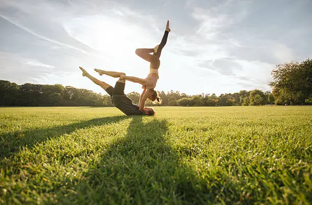 Healthy young couple doing acro yoga on grass. Man and woman doing various yoga poses in pair outdoors at the park.