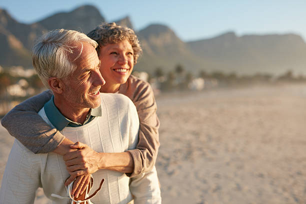 Senior couple enjoying their vacation at the beach Portrait of happy mature man carrying his beautiful wife on his back at the beach. Senior couple enjoying their vacation at the sea shore. jacob ammentorp lund stock pictures, royalty-free photos & images