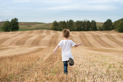Young boy running through freshly cut cropped field.  Symbolizes everything that youth is about, being fancy free and having nothing but opportunity in front of you.  