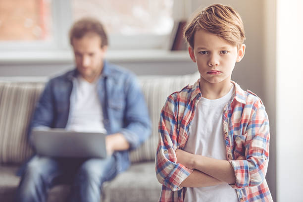 Father and son Sad little boy is looking at camera while his father is working in the background indifference stock pictures, royalty-free photos & images