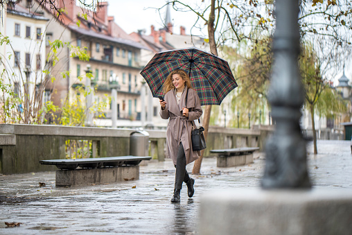 Happy woman with umbrella on a rainy day walking down the street