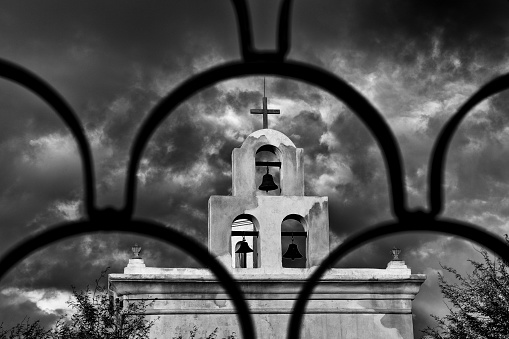 Cross and bells at San Xavier Mission, Tucson, Arizona, USA. San Xavier Mission is a Catholic mission founded in 1692. It is a national historic landmark located 9 miles south of downtown Tucson. The mission 's interior is filled with original statues and mural paintings of 18th century. It is a popular tourist destination.