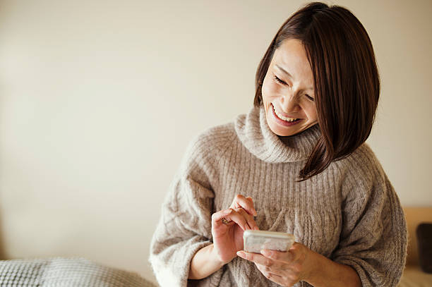 mujer adulta media usando un teléfono inteligente en la habitación de la cama - clothing satisfaction enjoyment day fotografías e imágenes de stock