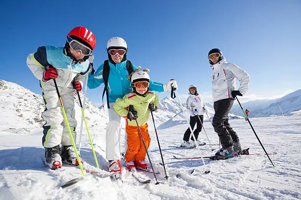 children and adults in skiing clothes with helmets and skis on ski slope