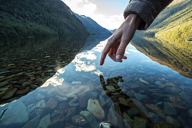 Finger touches surface of mountain lake, New Zealand Finger touches surface of mountain lake, the landscape is reflecting on the water. milford sound stock pictures, royalty-free photos & images