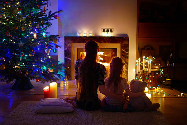 istock Young mother and daughters sitting by a fireplace on Christmas 626783312