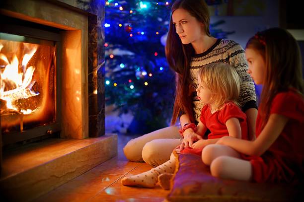 istock Young mother and daughters sitting by a fireplace on Christmas 626783348