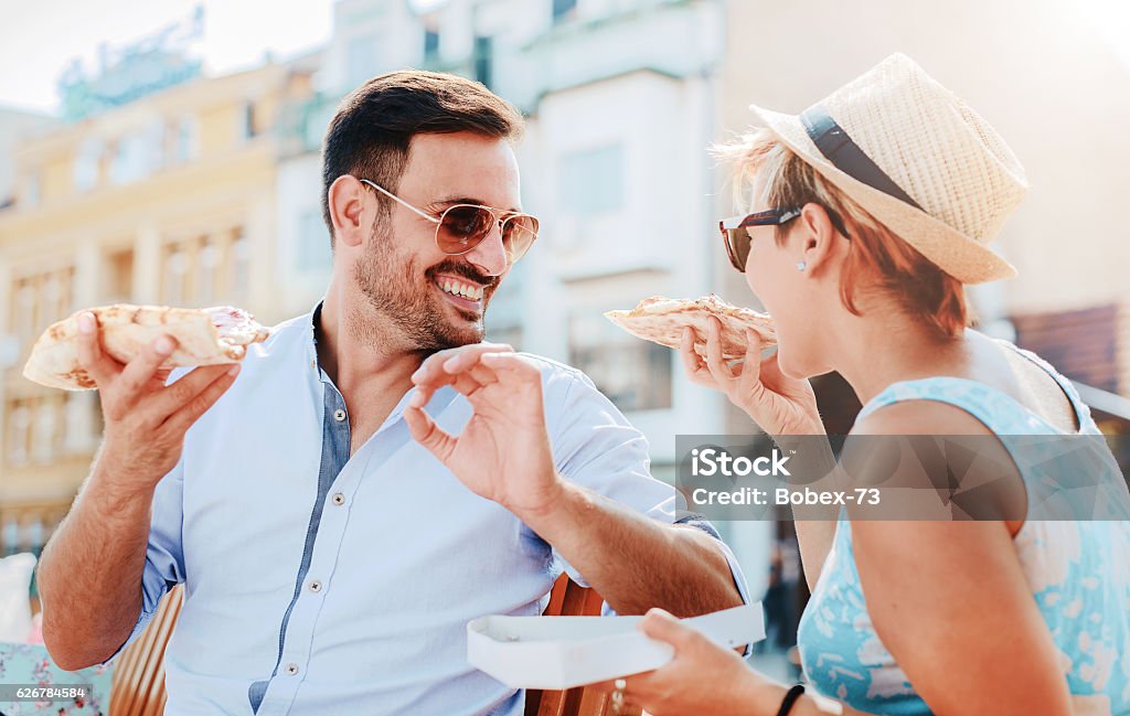 Loving couple eating pizza outdoors Beautiful loving couple sitting on the bench in the center of the city and eating pizza. Lifestyle concept Italy Stock Photo