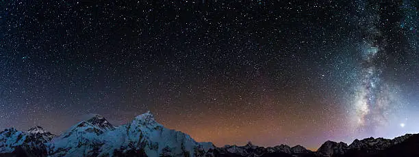 Milky Way and stars shining above the iconic summit pyramid of Mt. Everest (8848m) and the snow capped mountain peaks of the Khumbu Himalaya deep in the Sargamatha National Park of Nepal, a UNESCO World Heritage Site.