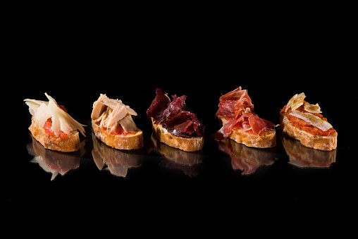 Variety of toasts over black background with reflection. Spanish creative tapas