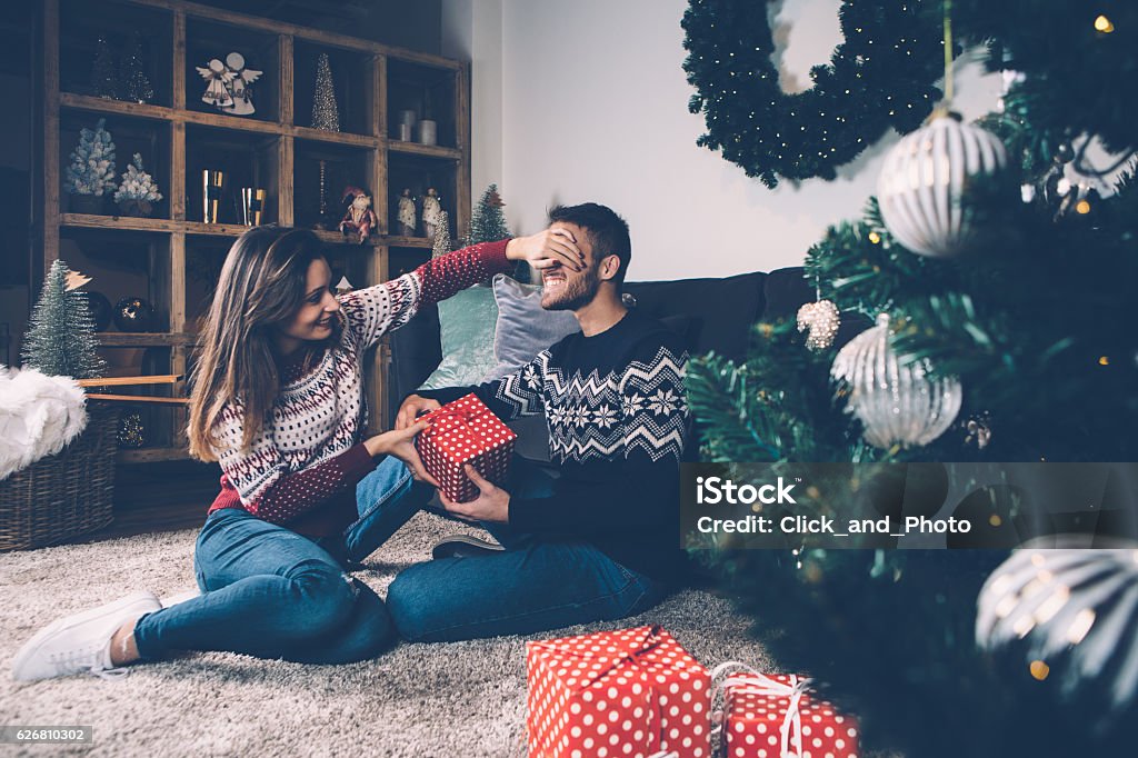 Mujer cerrando los ojos al novio dando regalo - Foto de stock de Regalo de navidad libre de derechos