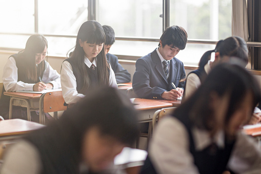 High school students studying in classroom. Schoolboys and girls are attending lecture in brightly lit school. All are wearing uniforms.