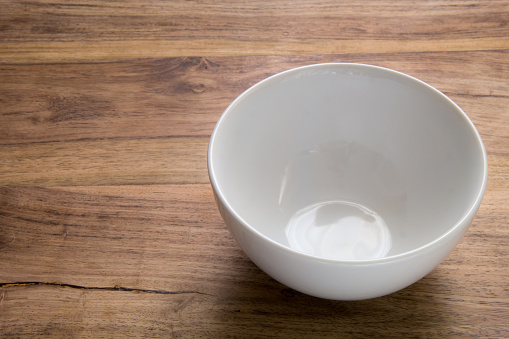 A simple picture of an empty white plate on a rustic wooden table bathed in natural light. Uncluttered. Space to the side of the vessel for text (if required).
