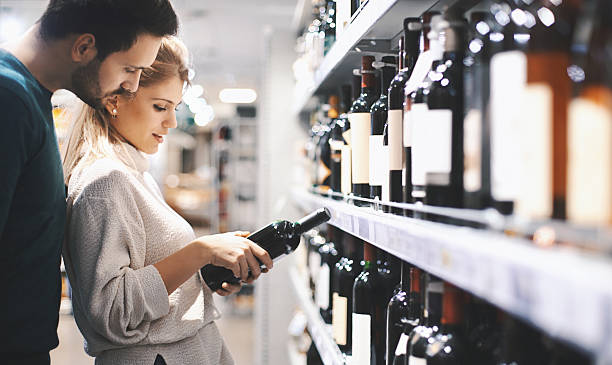 Couple buying wine in supermarket. Closeup of early 30's couple doing some home shopping in local supermarket. They are walking down wine aisle and choosing a bottle of red wine. Side view. alcohol shop stock pictures, royalty-free photos & images
