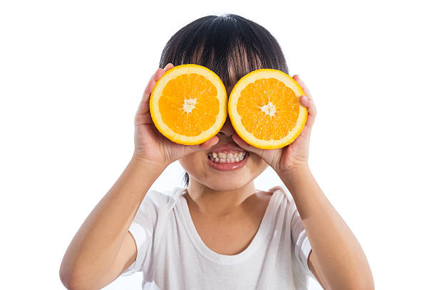 Happy Asian Chinese little girl using orange as glasses Happy Asian Chinese little girl using orange as glasses in isolated white background. oranges with faces stock pictures, royalty-free photos & images