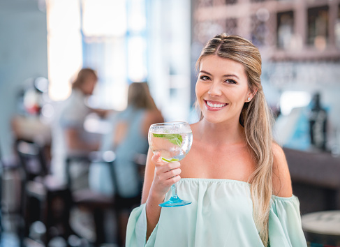 Beautiful young woman having drinks at a restaurant and looking at the camera smiling