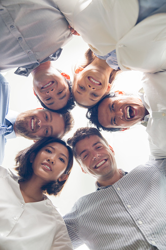 Below view of young multiethnic business team, embracing, looking at camera and smiling