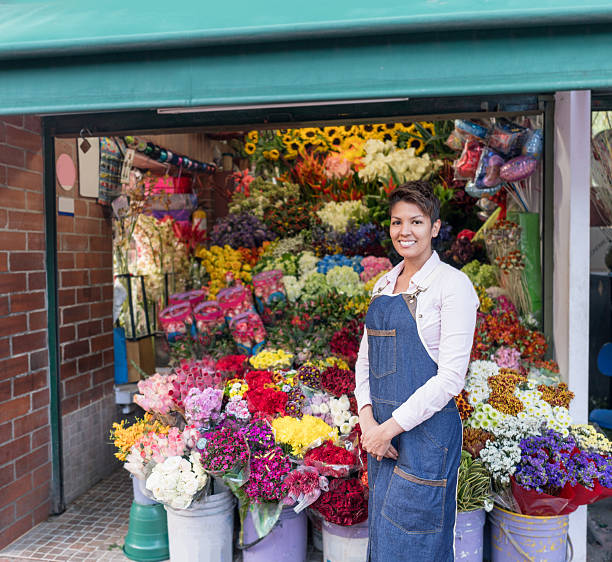 Happy female entrepreneur selling flowers at a stand and looking at the camera smiling