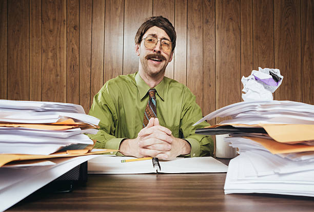 Cliche Office Salesman A white collar business man working in a retro 1980's style office sits at a desk piled with paperwork and documents.  He looks at the camera with a cheesy smile while making his sales pitch. kitsch photos stock pictures, royalty-free photos & images