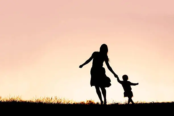 Photo of Silhouette of Mother and Baby Daughter Running and Dancing at Sunset