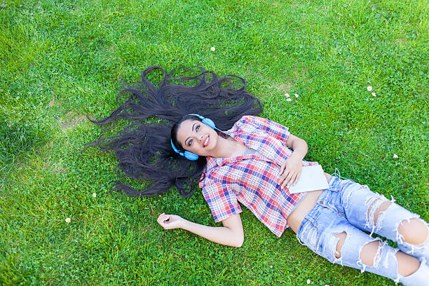 istock Smiling young woman listening music lying down on grass 626867704