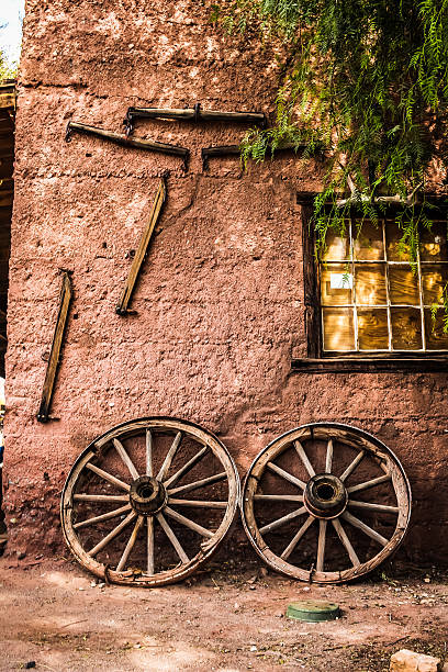 An old wagon wheel rests against a sandstone wall.