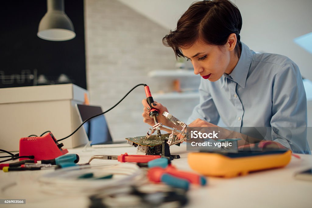 Woman Soldering a circuit board in her tech office. Close up of female engineer using solder in her office. Testing and fixing a circuit board. Electronics Industry Stock Photo