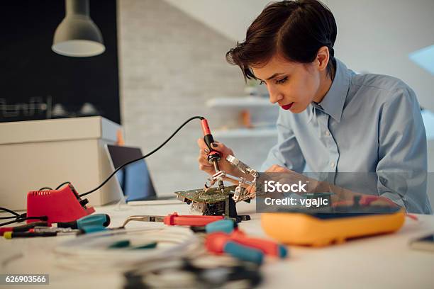 Woman Soldering A Circuit Board In Her Tech Office Stock Photo - Download Image Now