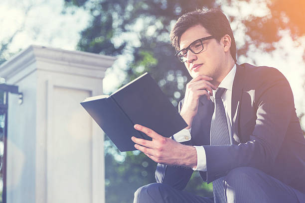 istock Thoughtful businessman reading book outside, toned 626905316