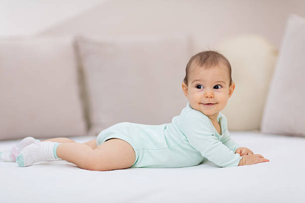 Baby girl on white bed Cute baby girl lying on her tummy bear stomach stock pictures, royalty-free photos & images