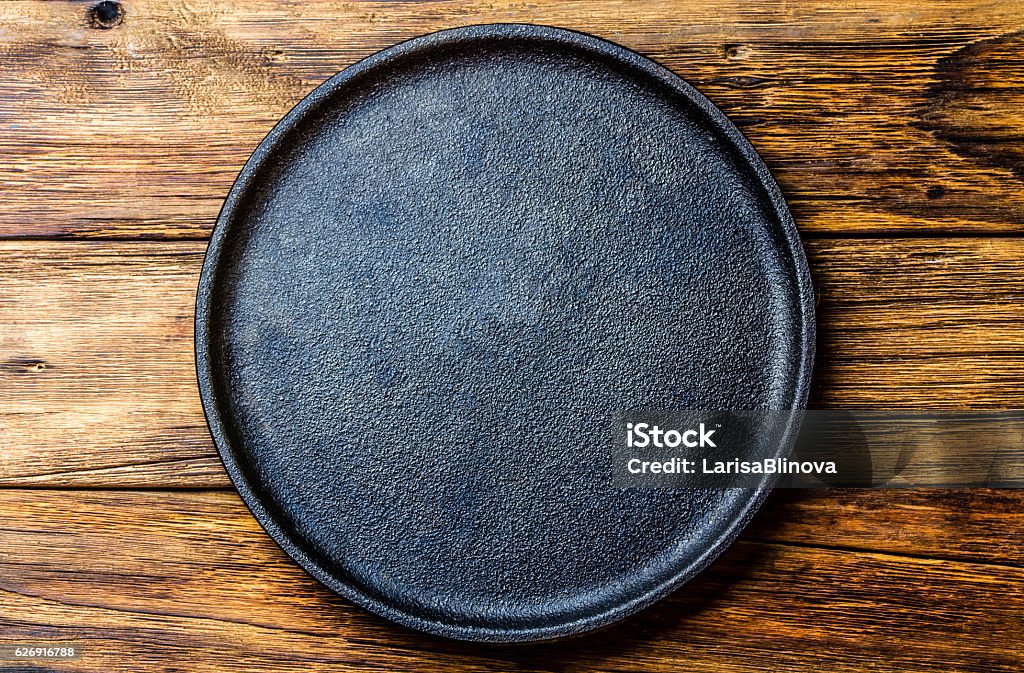 Leere rustikale schwarze Gusseisenplatte über altem Holzhintergrund - Lizenzfrei Teller Stock-Foto