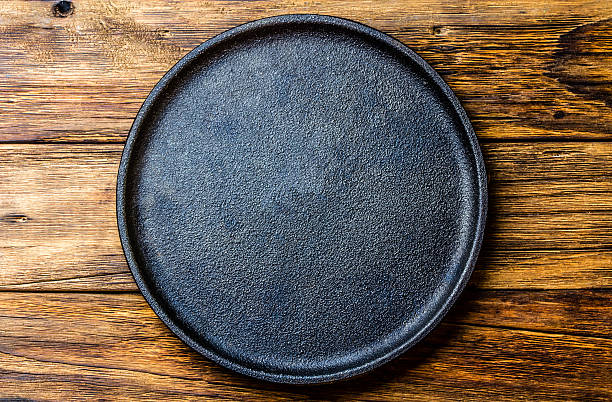 Empty rustic black cast iron plate over old wooden background