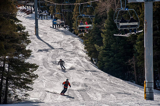 Sipapu, New Mexico, USA - February 28, 2012: Two Skiers Race down Slope More Ride Ski Lift on a nice sunny blue bird day in the Sangre De Cristo Mountains during Snow Season a great day for winter sports