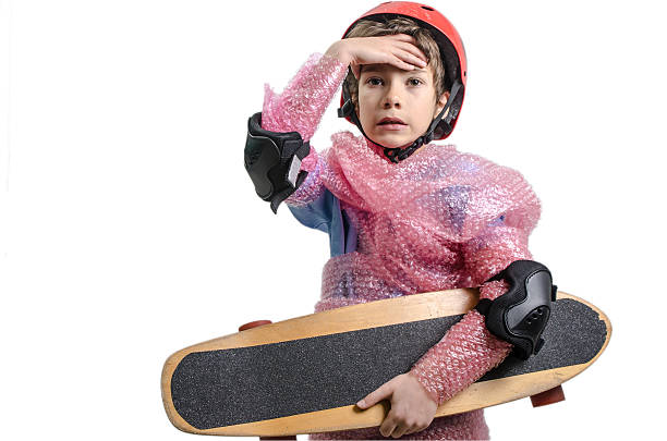 Kid with skateboard wrapped in plastic bubble by overprotecting parent.