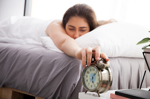 Woman reaching out hands and trying to turn off alarm in the morning