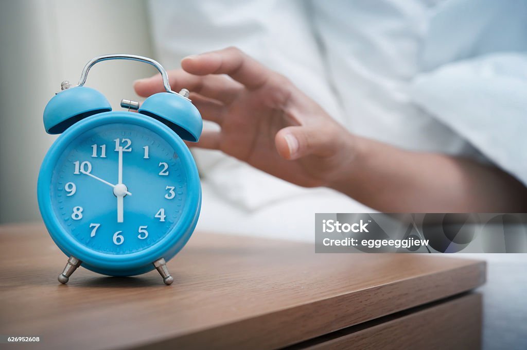 Early morning. Woman hand reaching out bed for retro alarm clock. Early morning. Alarm Clock Stock Photo