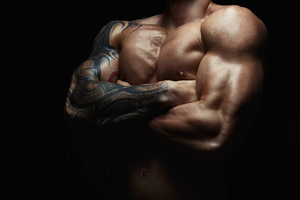 Strong athletic man showes naked muscular body Athletic man's torso. Unrecognizable male fitness model show naked muscular body. Strong hands, chest and shoulder muscles and biceps. Studio shot on black background, low key. Bodybuilding concept man muscular chest stock pictures, royalty-free photos & images