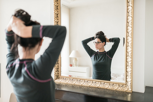 Woman standing in front of the mirror and tying her hair