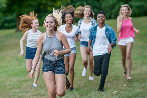 Playing Tag A multi-ethnic group of teenagers are hanging out together at the park on a sunny summer day. They are playing tag and running through the grass. teenagers only teenager multi ethnic group student stock pictures, royalty-free photos & images