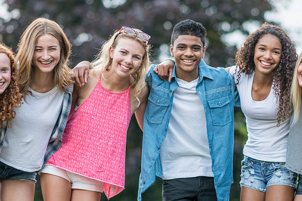 Friends Standing Together Outside A multi-ethnic group of teenagers are hanging out together at the park on a sunny summer day. They are standing in a row and are smiling while looking at the camera. teenagers only stock pictures, royalty-free photos & images