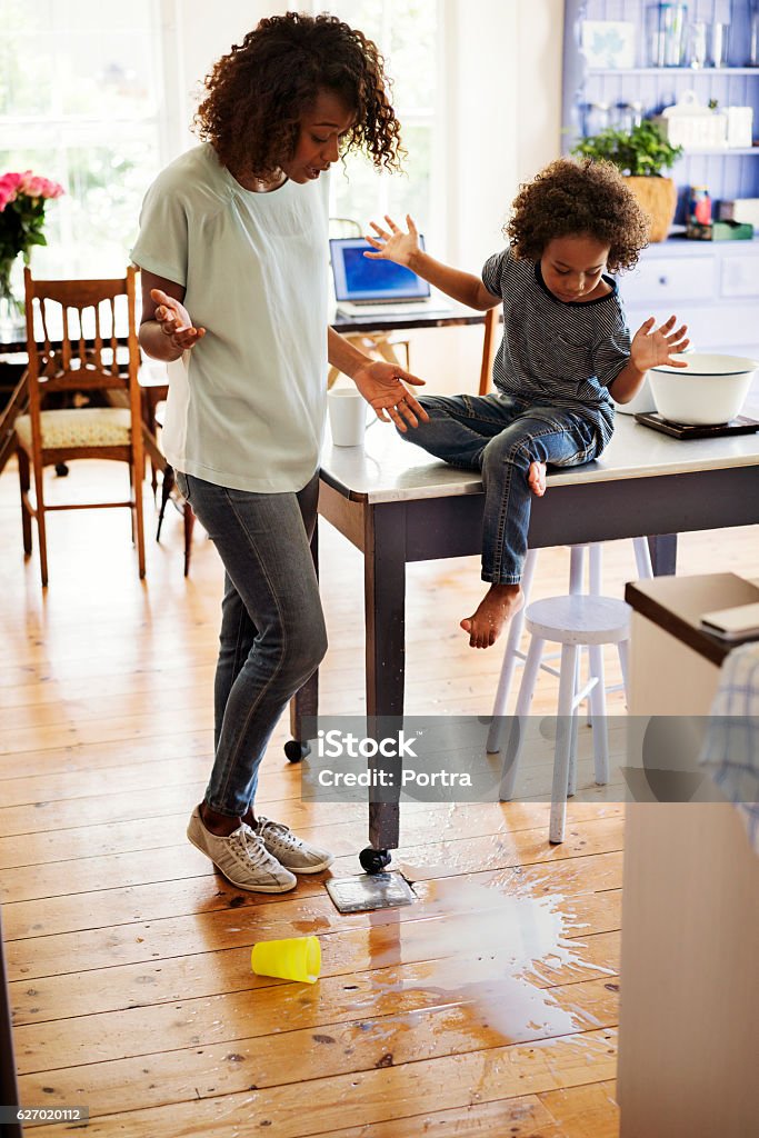 Shocked mother and son looking at fallen milk A photo of shocked mother and son looking at fallen milk on floor. Amazed woman and boy are gesturing at home. They are in casuals. Messy Stock Photo