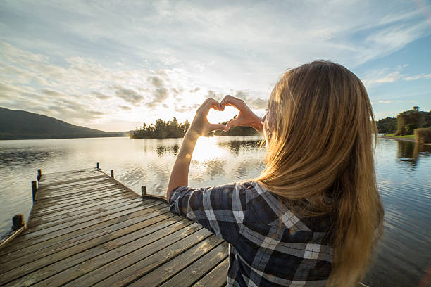 istock Woman on pier makes heart shape frame against sunset 627021346