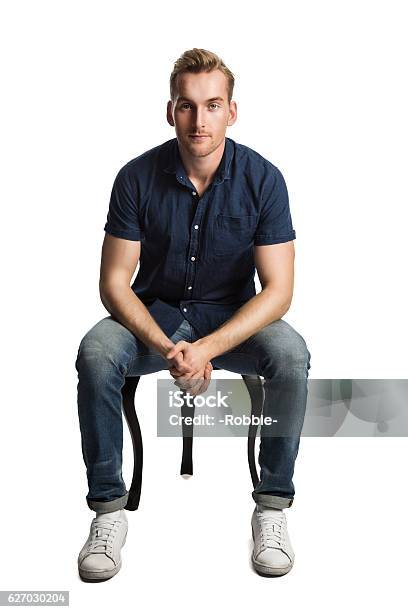 Man In Blue Shirt And Jeans Sitting Down Stock Photo - Download Image Now - Sitting, Men, White Background
