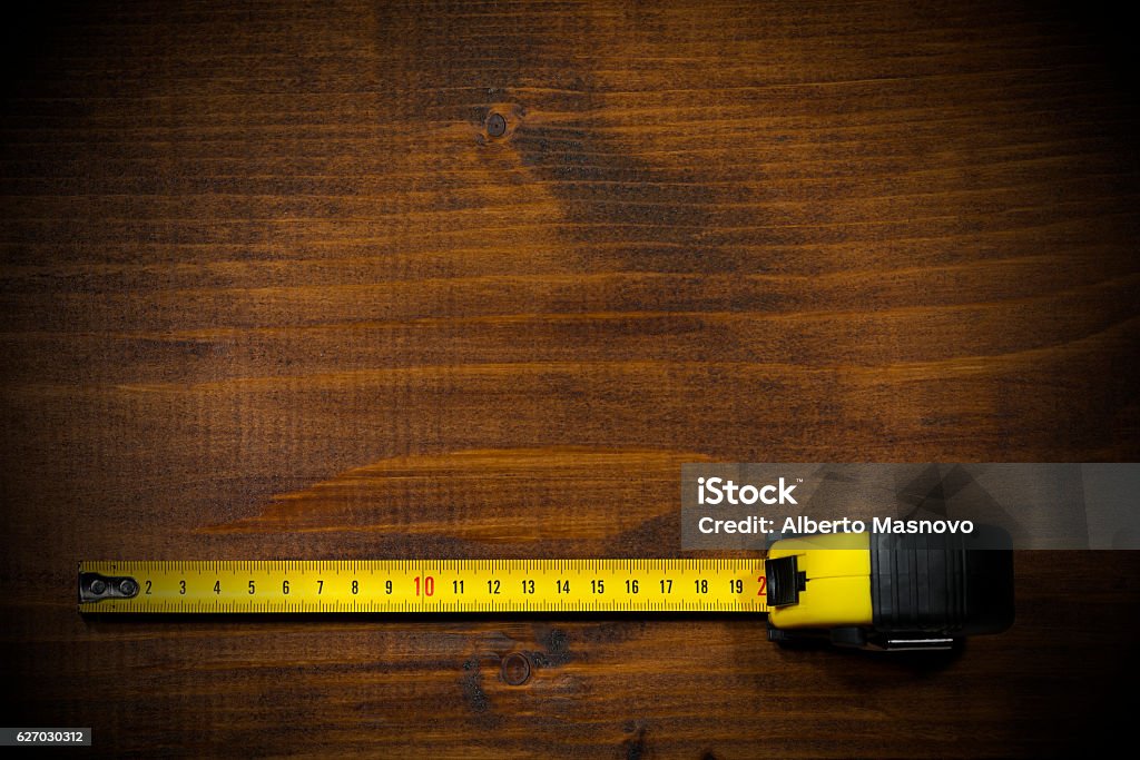 Tape Measure on a Wooden Work Table Yellow and black tape measure on a wooden and empty work table with dark shadows Measuring Stock Photo